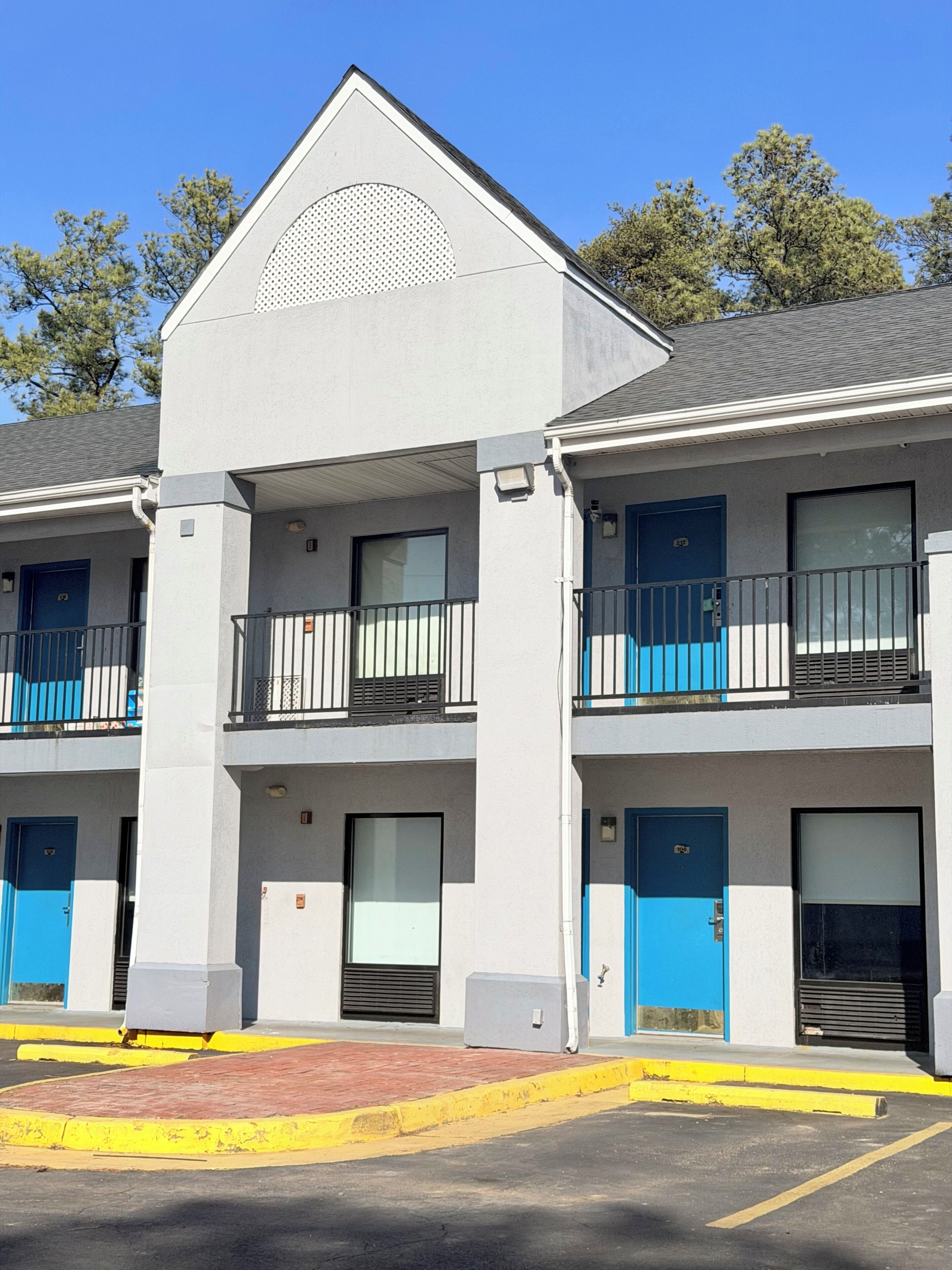 A multi-story building with balconies, blue doors, and a parking lot.