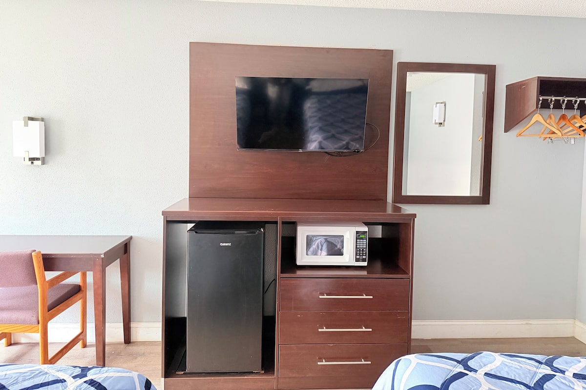 A hotel room with a bed, a desk, a refrigerator, a microwave, a television, and a wardrobe.