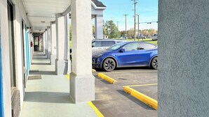 Ein überdachter Gang mit Säulen, der zu einem Parkplatz mit einem blauen Auto führt.