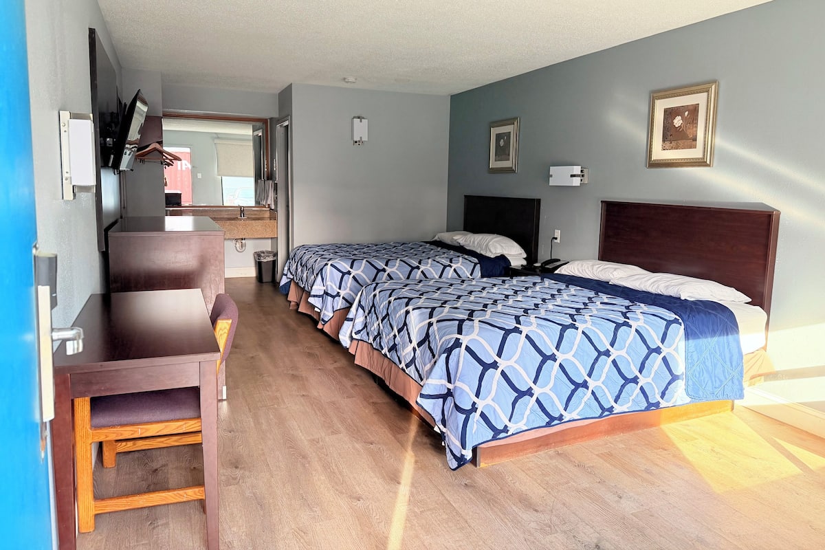A hotel room with two beds, a desk, and a mirror.