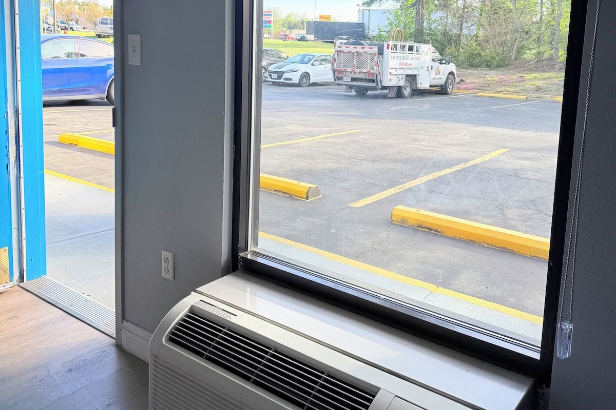A room with a large window, a wall-mounted air conditioner, and a door leading outside.