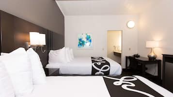 Une chambre d’hôtel avec deux lits, un bureau, une chaise, une lampe et une œuvre d’art accrochée au mur.