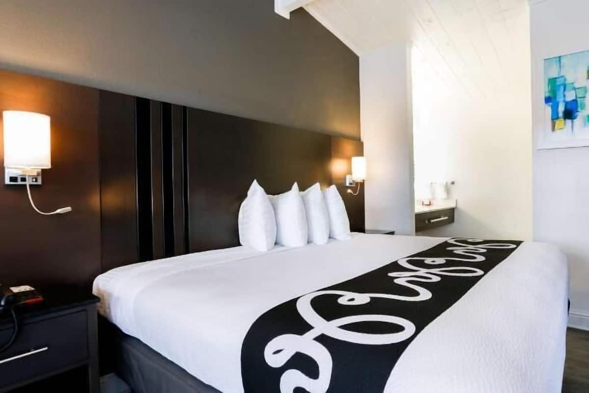Hotelkamer met een groot bed, nachtkastje, wandlamp, schilderij en een blauwe stoel.