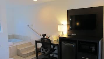 A hotel room with a desk, chair, TV, microwave, and a small bathroom with a bathtub and toilet.