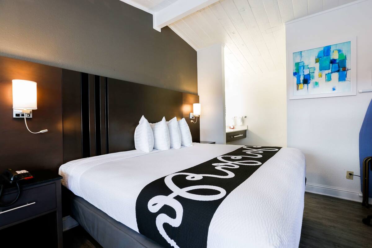 Een hotelkamer met een groot bed, een nachtkastje met een telefoon, een wandlamp en een schilderij.