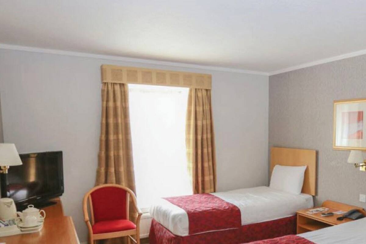 A hotel room with a bed, a desk with a chair, a television, and a window with curtains.