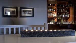 A bar area with a granite countertop, framed pictures on the wall, and a variety of bottles and glasses on shelves. - The Hickstead Hotel (Haywards Heath)