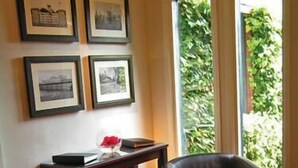 A room with two leather chairs, a small table, and a window with a view of greenery. - The Hickstead Hotel (Haywards Heath)
