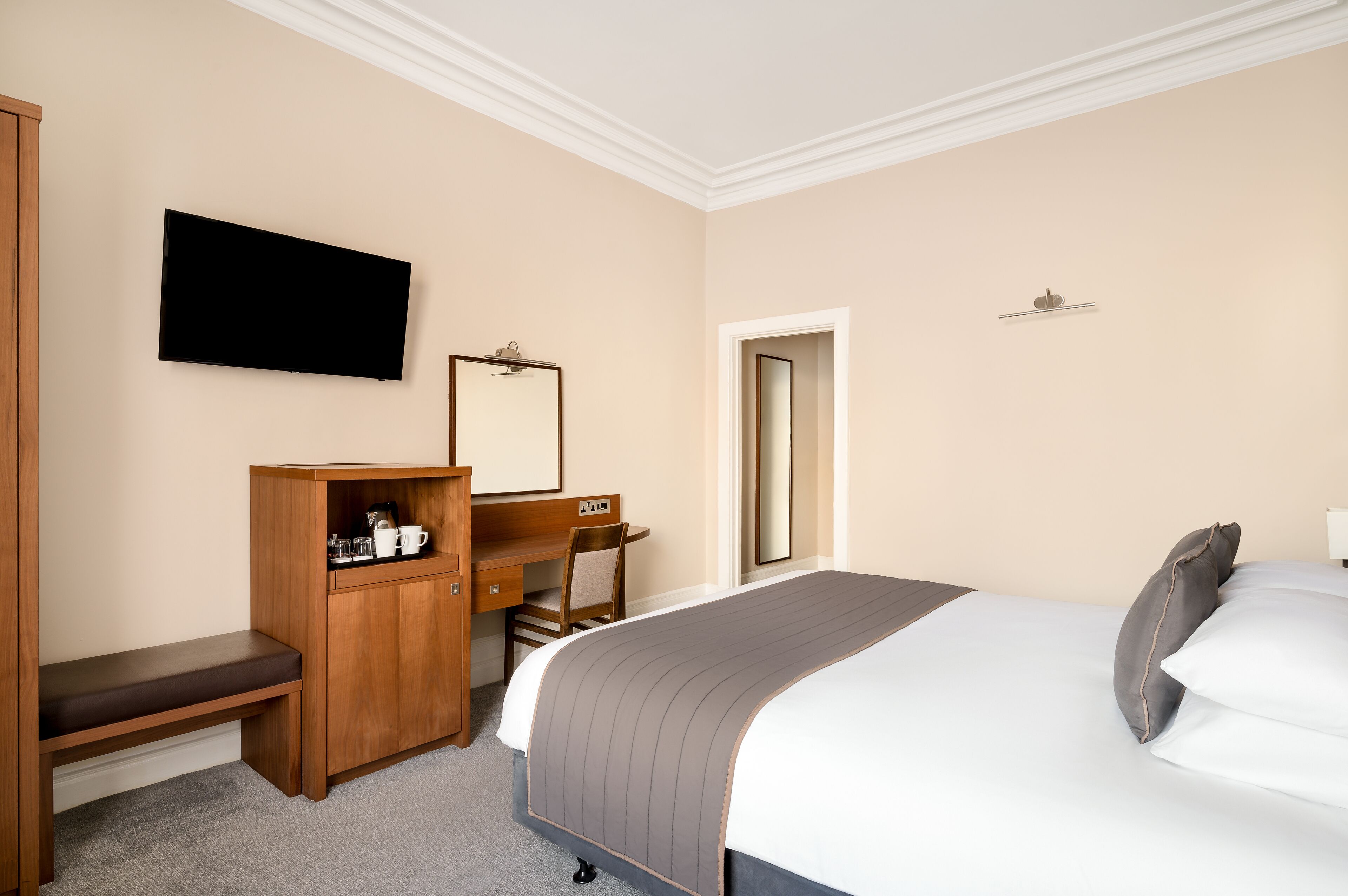 A hotel room with a bed, a desk, a chair, a television, and a wardrobe.