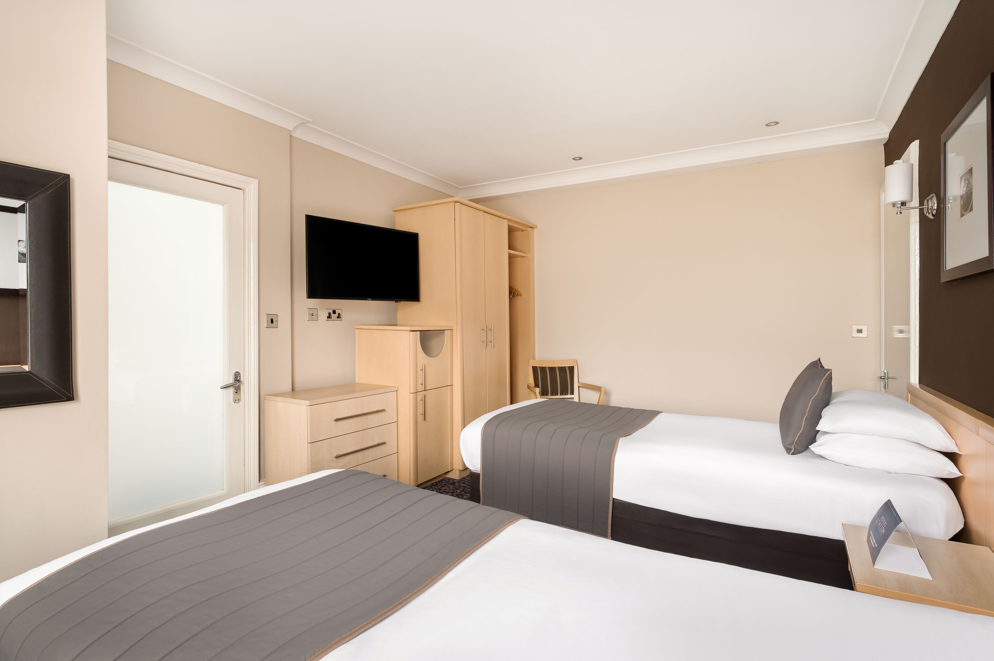 A hotel room with two beds, a TV, a wardrobe, and a desk.