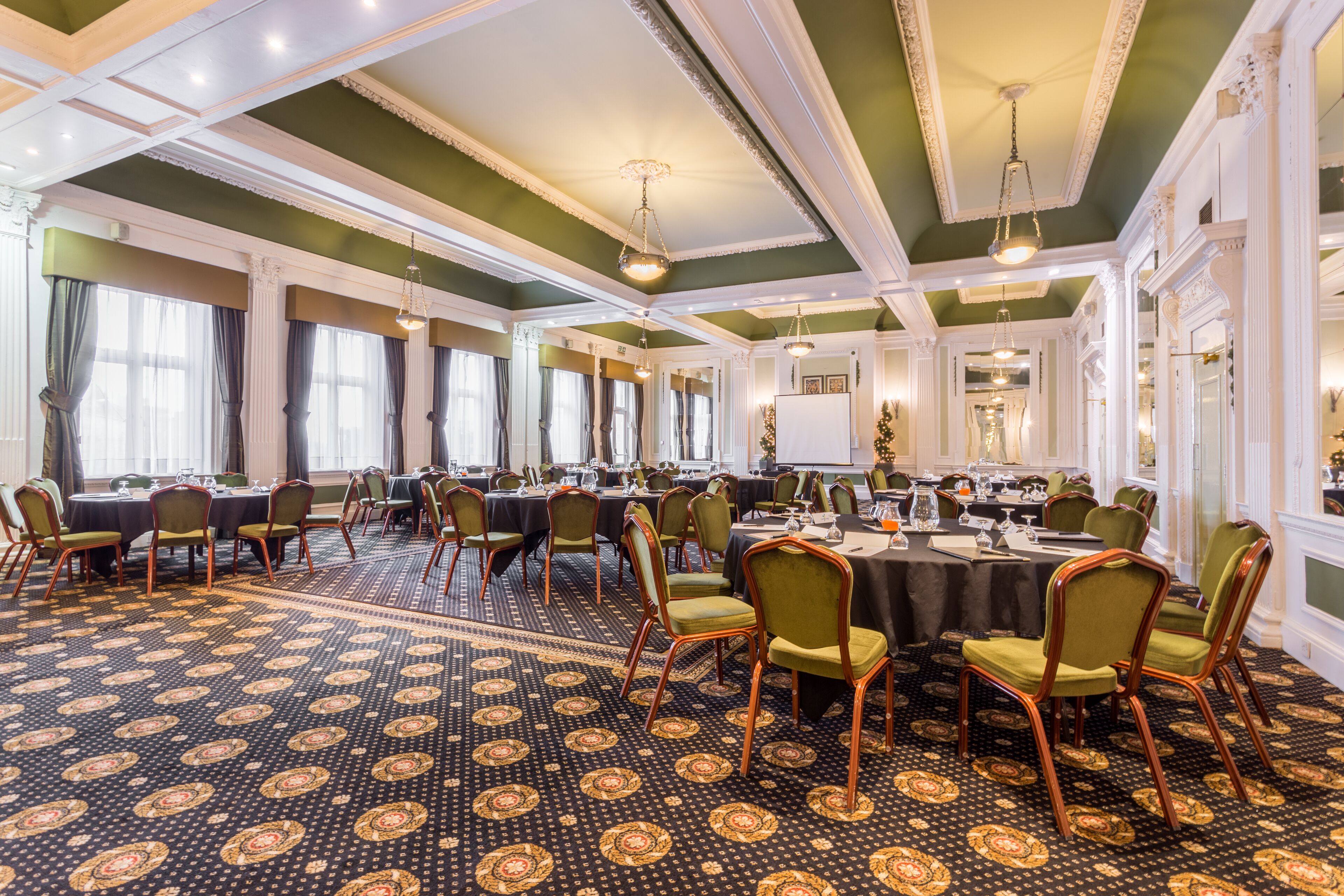 A conference room with round tables, green chairs, and patterned carpet.