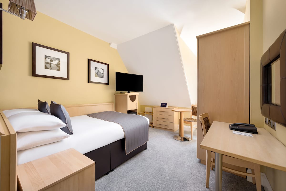 Een hotelkamer met een bed, bureau, stoel, televisie en twee foto's in lijsten aan de muur.