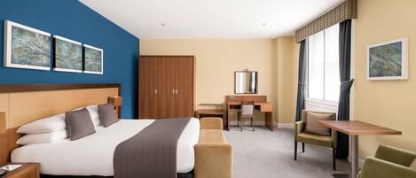 A hotel room with a large bed, a desk, a chair, and a small table.