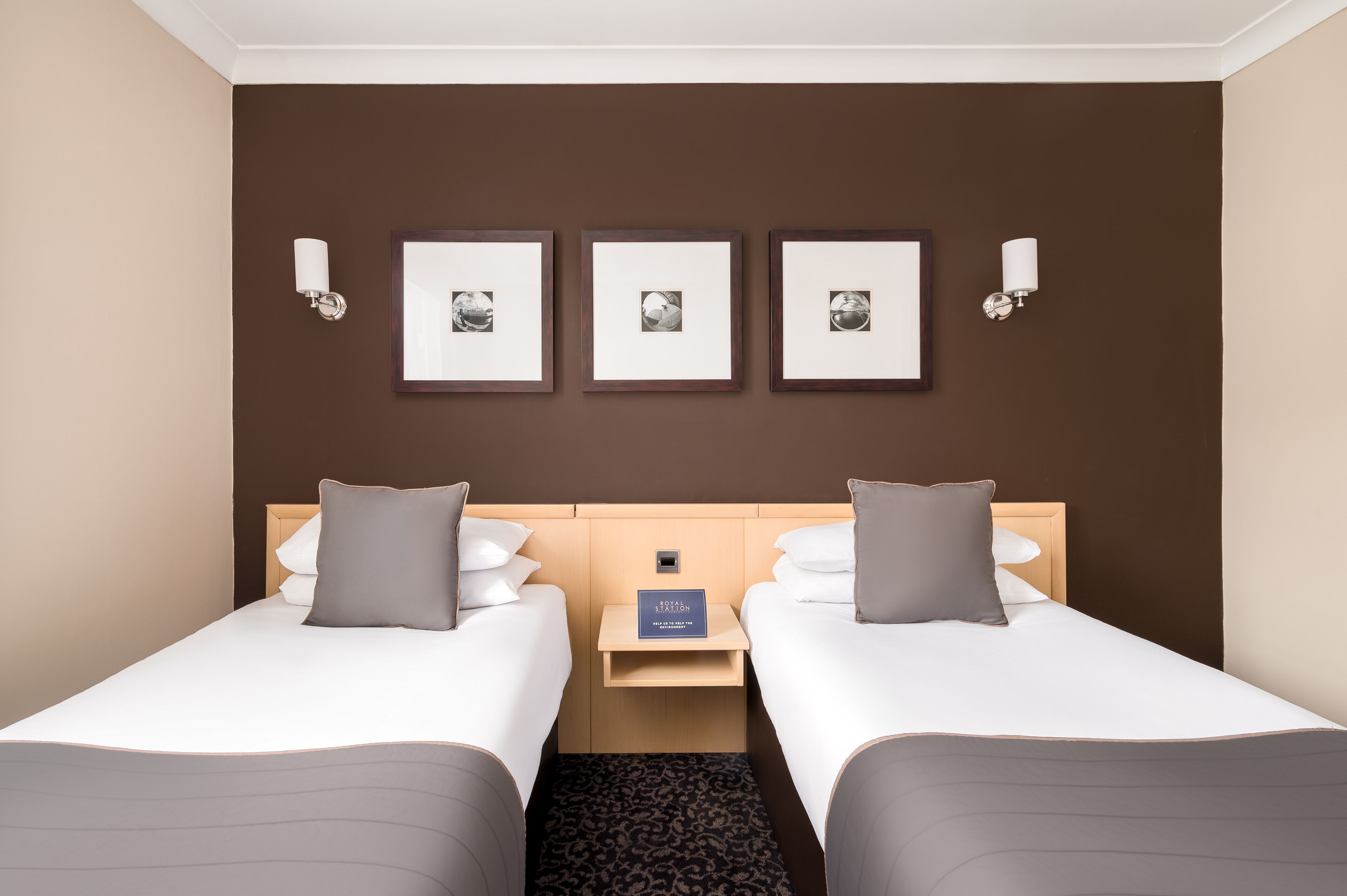 A hotel room with two beds, a nightstand, and three framed pictures on the wall.