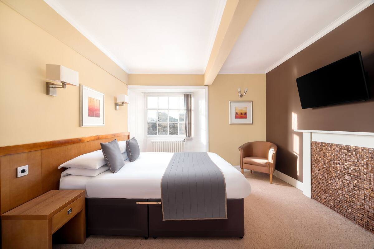 Een hotelkamer met een bed, nachtkastje, stoel, televisie en kunstwerken aan de muur.