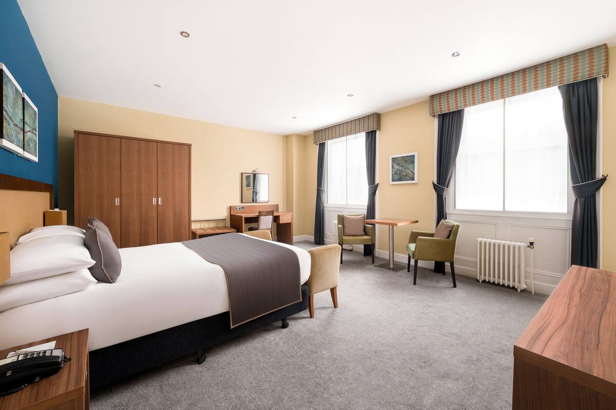Hotelkamer met een bed, bureau, stoel, radiator en raam met gordijnen.