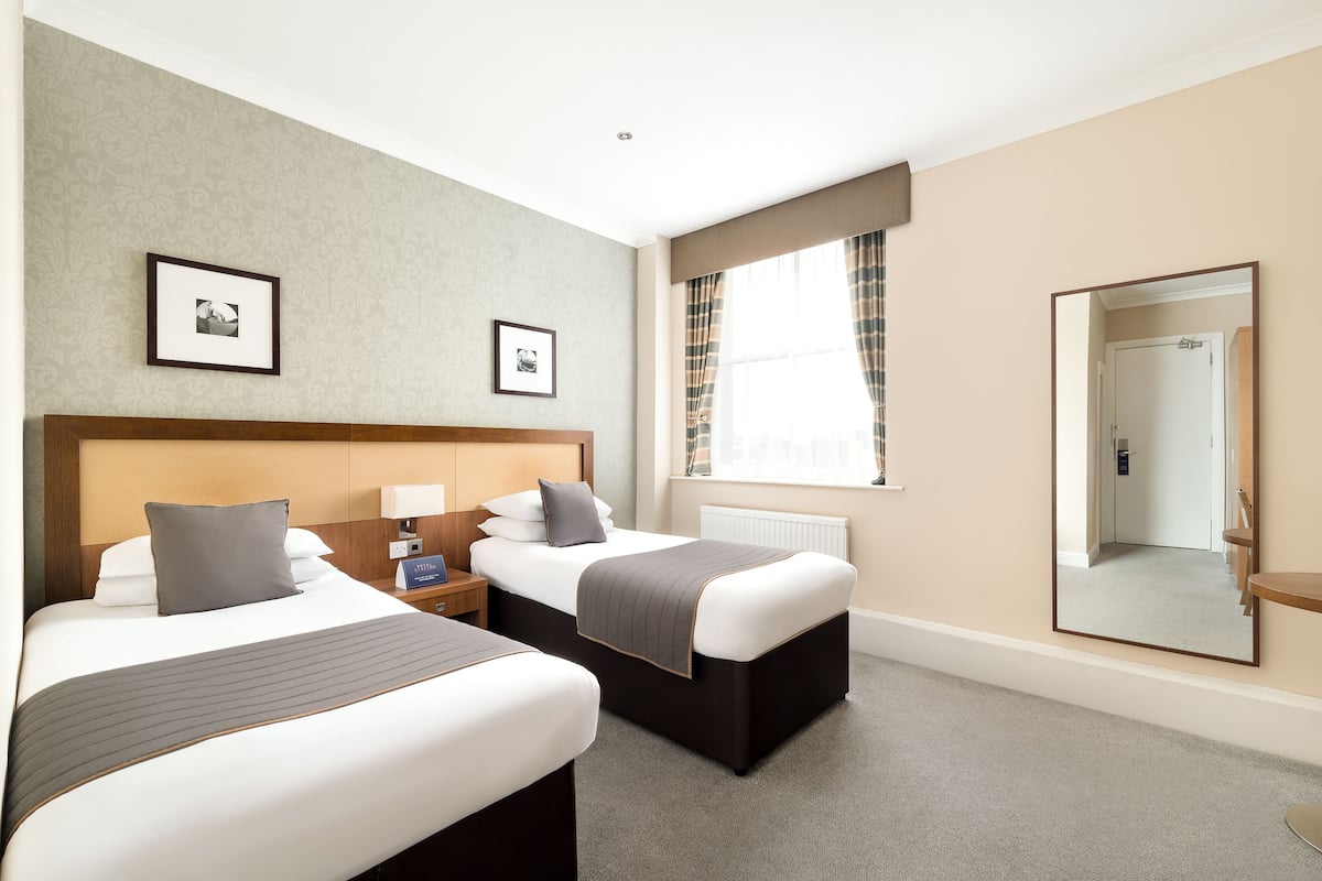 Een hotelkamer met twee bedden, een grote spiegel en een raam met gordijnen.