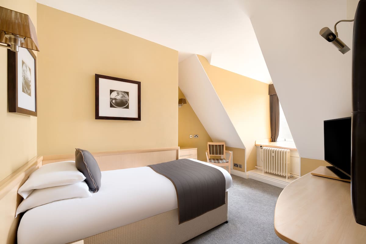 Een hotelkamer met een bed, een stoel, een televisie en een lijst met een afbeelding aan de muur.