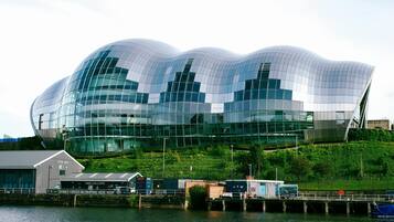 A modern glass building with a wavy roof, situated by a waterfront.