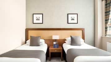 A hotel room with two beds, a wooden headboard, a nightstand with a lamp, and framed pictures on the wall.
