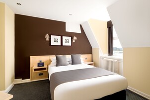 Quarto de hotel moderno com uma cama grande, uma mesa de cabeceira, uma luminária na parede e uma janela com vista.