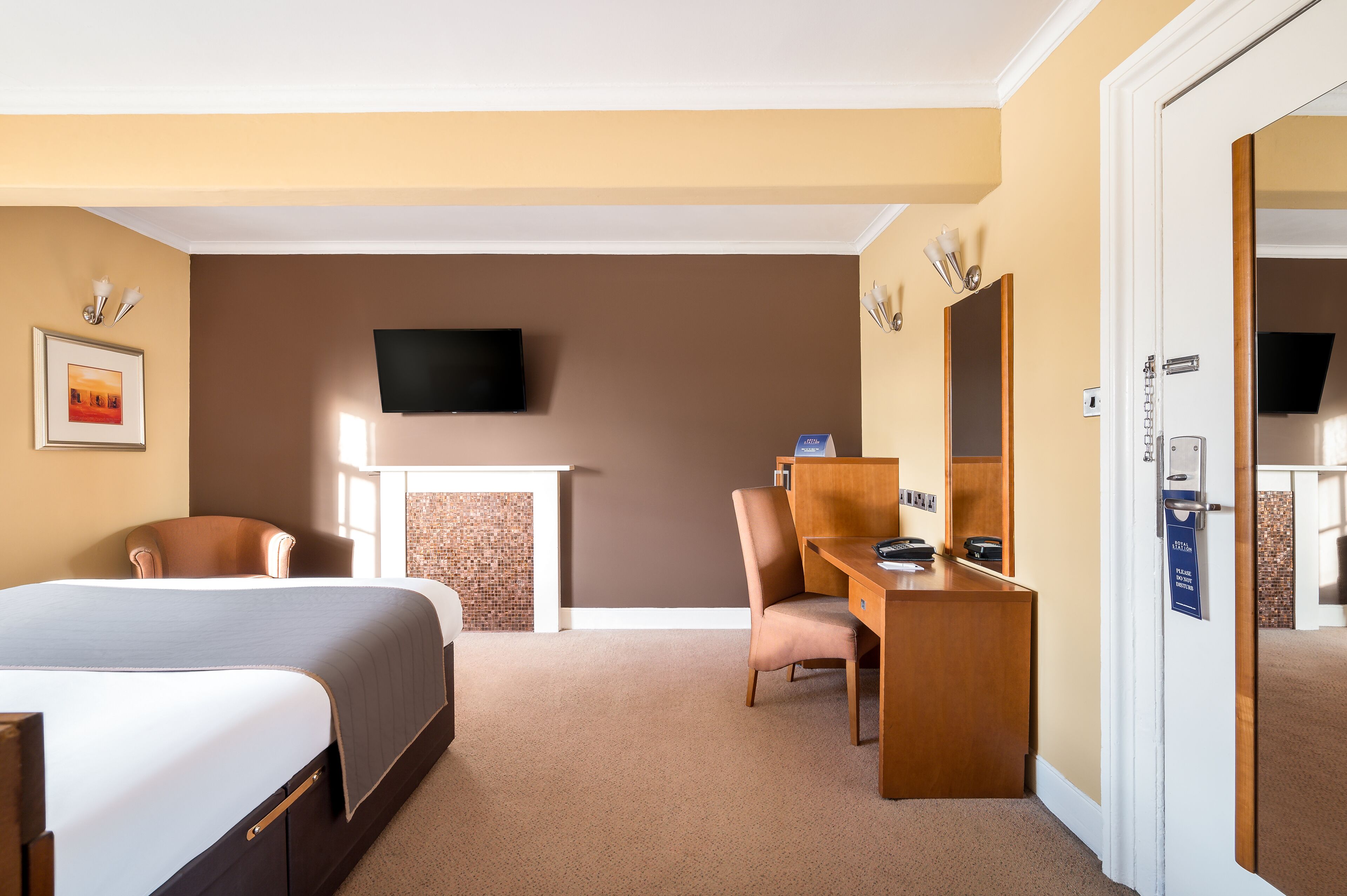 A hotel room with a bed, a desk, a chair, a television, and a fireplace.