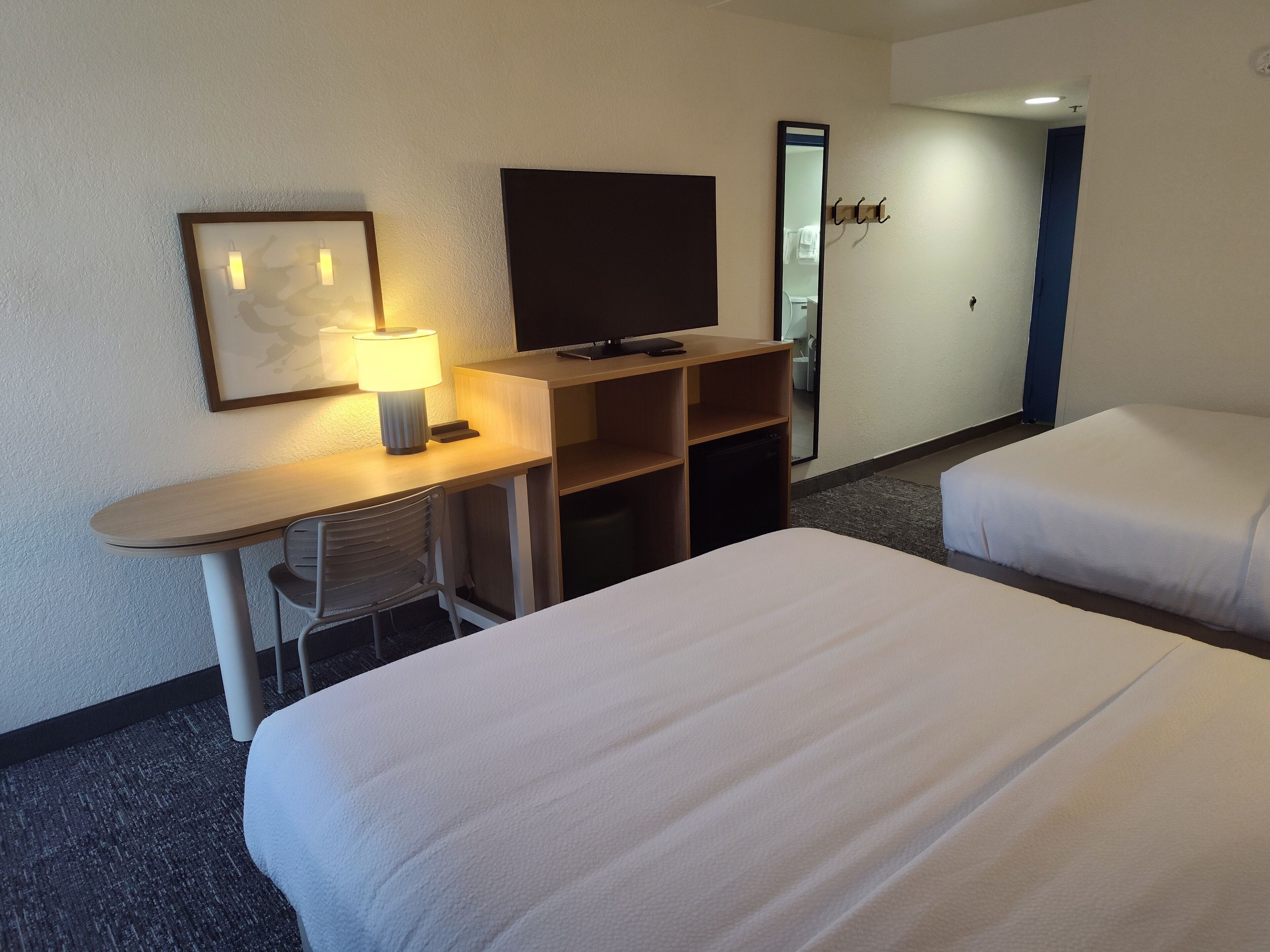 Habitación de hotel con dos camas, un escritorio con lámpara, televisión y espejo.