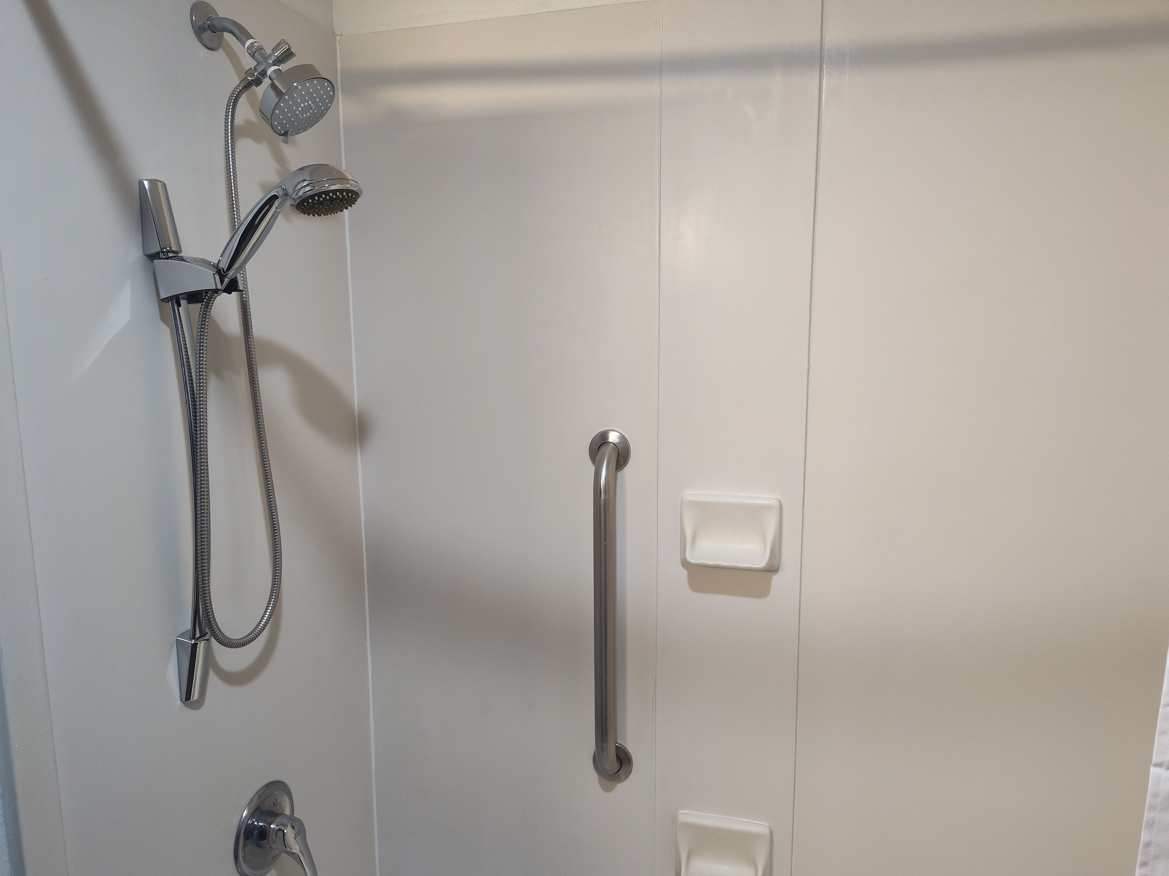 A bathroom with a shower, grab bars, and a toilet.