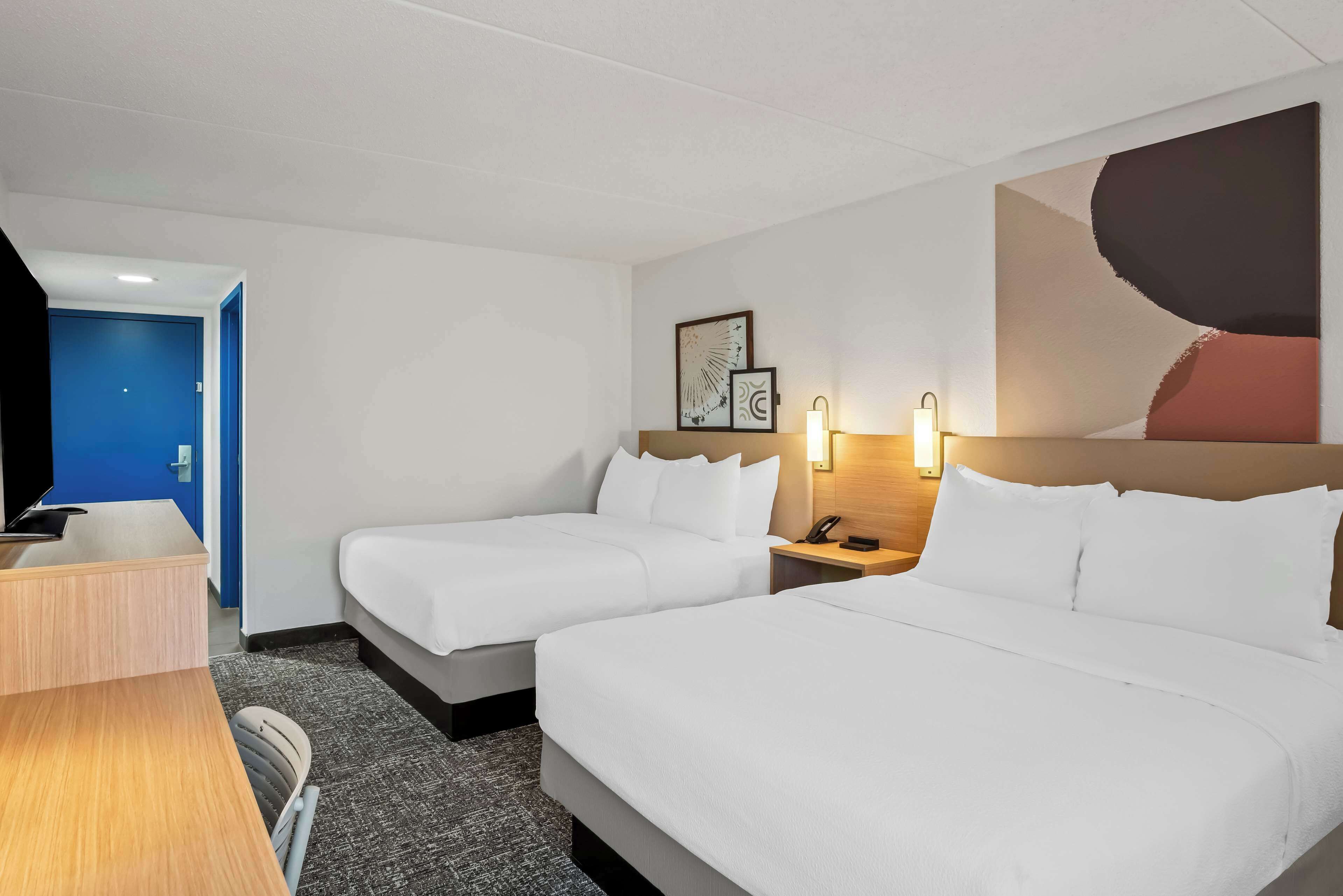 Une chambre d’hôtel avec deux lits, un bureau, une télévision et une porte bleue.