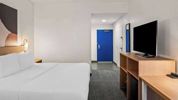 Habitación de hotel con cama, escritorio con televisor, puerta azul y mesita de noche con lámpara.