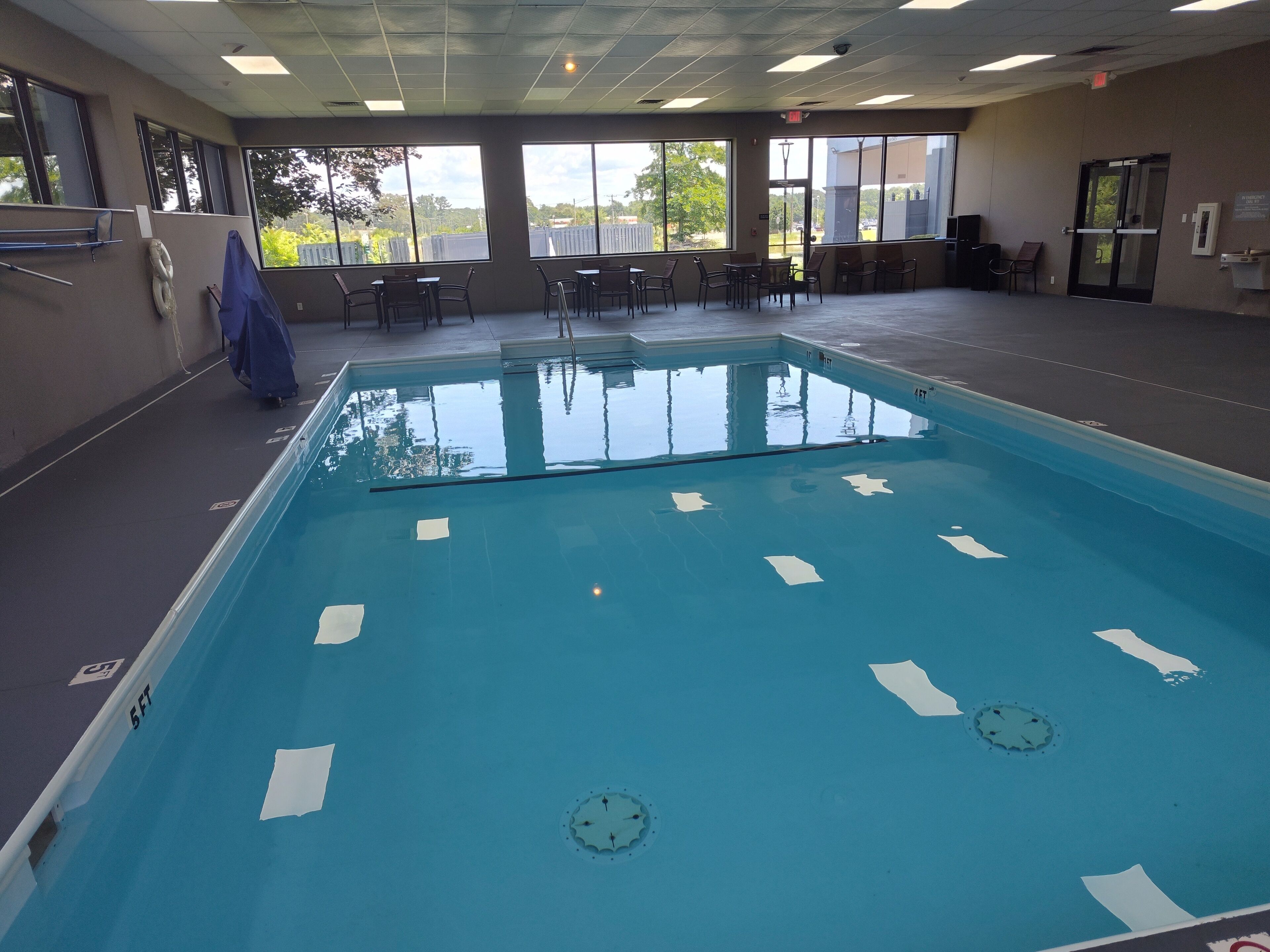 An indoor swimming pool with clear water, surrounded by windows and chairs.