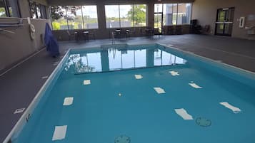 An indoor swimming pool with clear water, surrounded by windows and chairs.