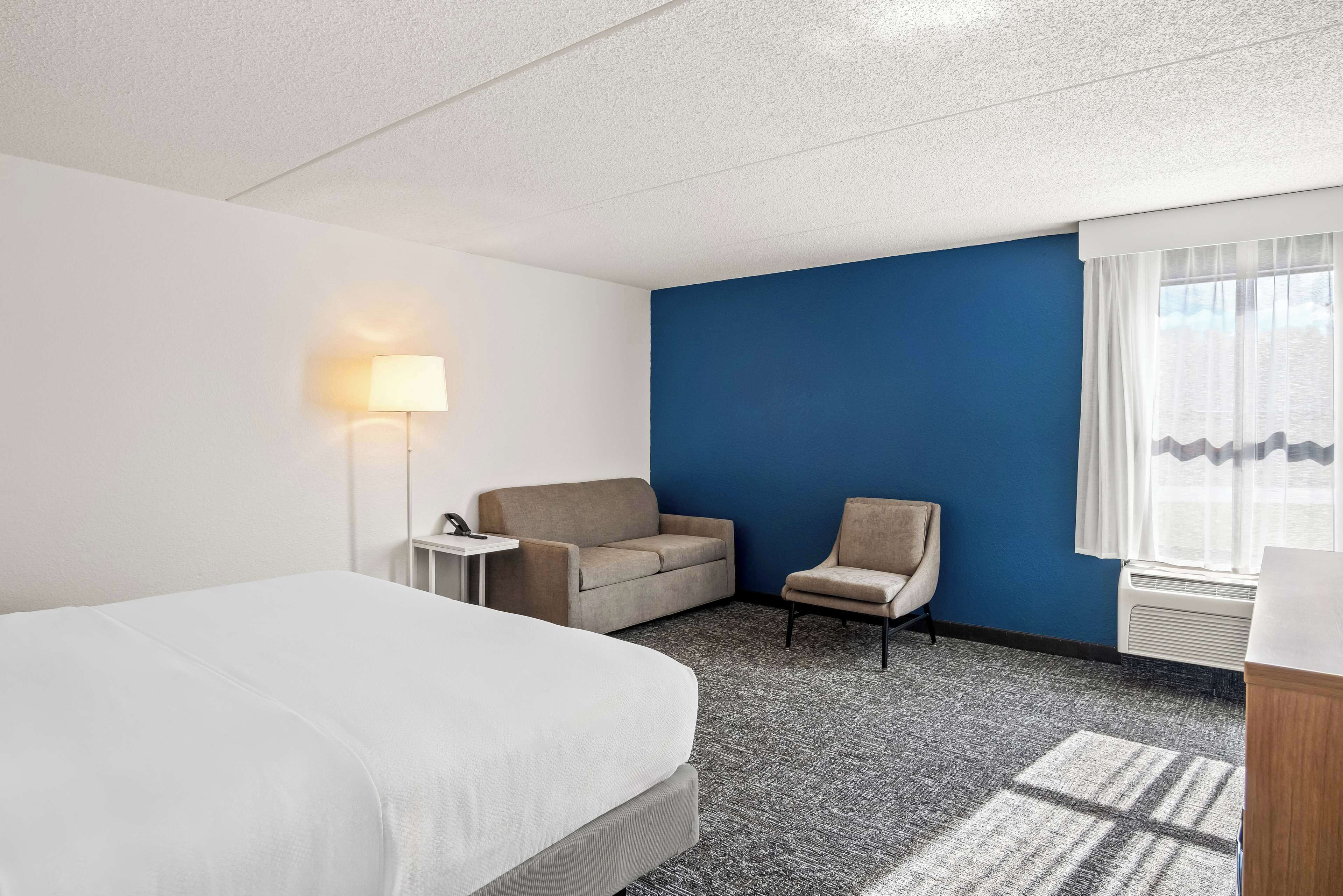A hotel room with a bed, a sofa, a chair, a lamp, and a window with curtains.