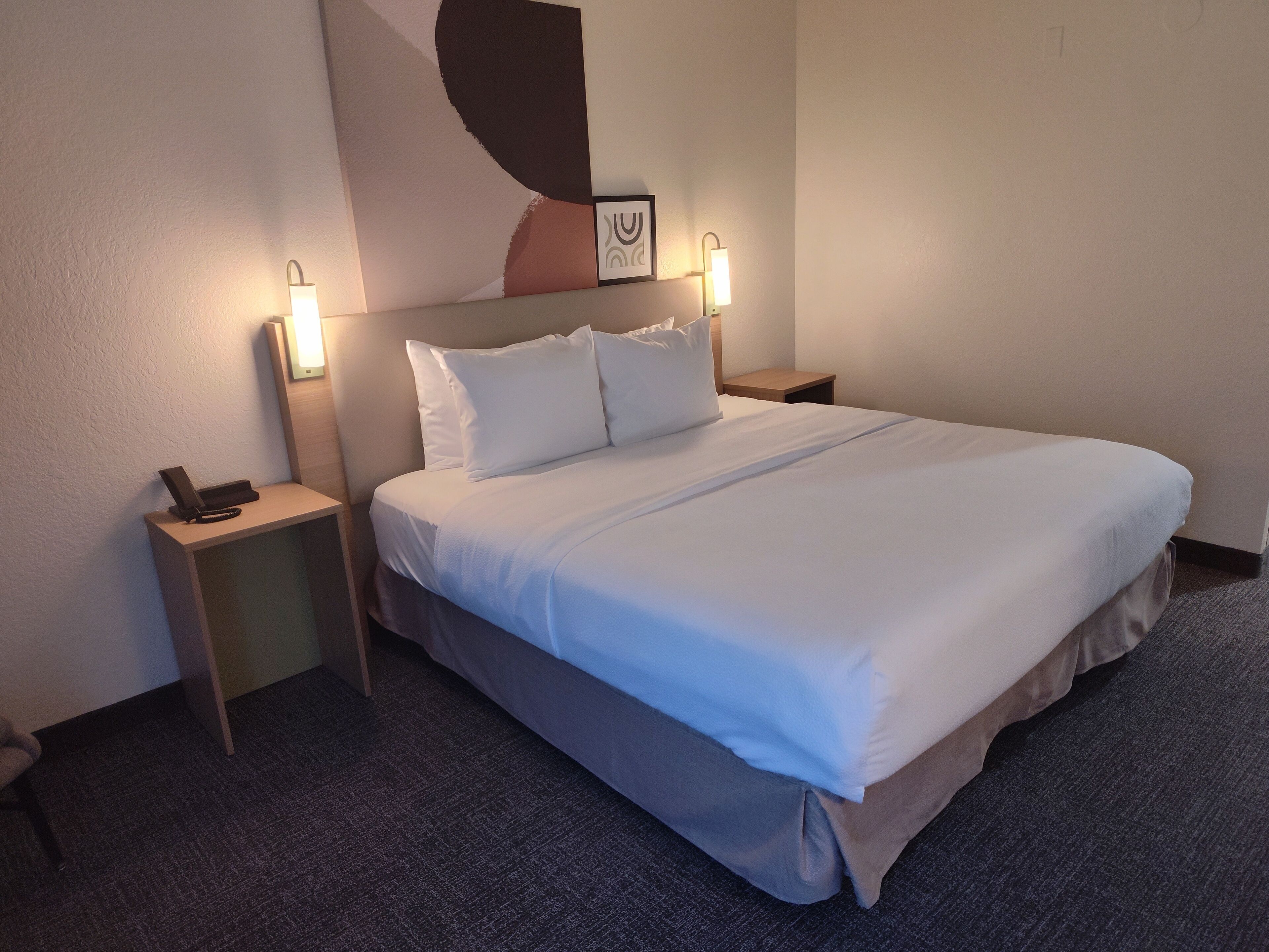 A neatly made bed with white linens, two bedside tables with lamps, and a wall-mounted artwork.