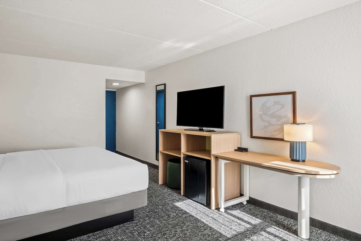 Ett hotellrum med en säng, ett skrivbord med en dator, en tv och en lampa.