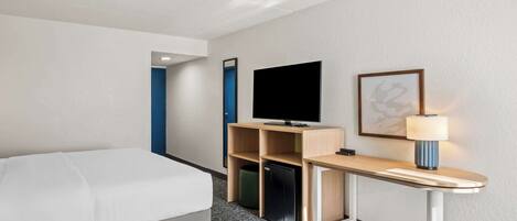 Una habitación de hotel con una cama, un escritorio con ordenador, un televisor y una lámpara.