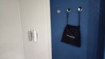Un baño con una puerta blanca y una pared azul. Hay dos botellas de productos para el cabello en la pared y un bolso negro con la etiqueta 'HAIR DRYER' colgado allí.