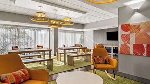 A modern hotel lobby with a dining area, comfortable seating, and a large artwork on the wall.