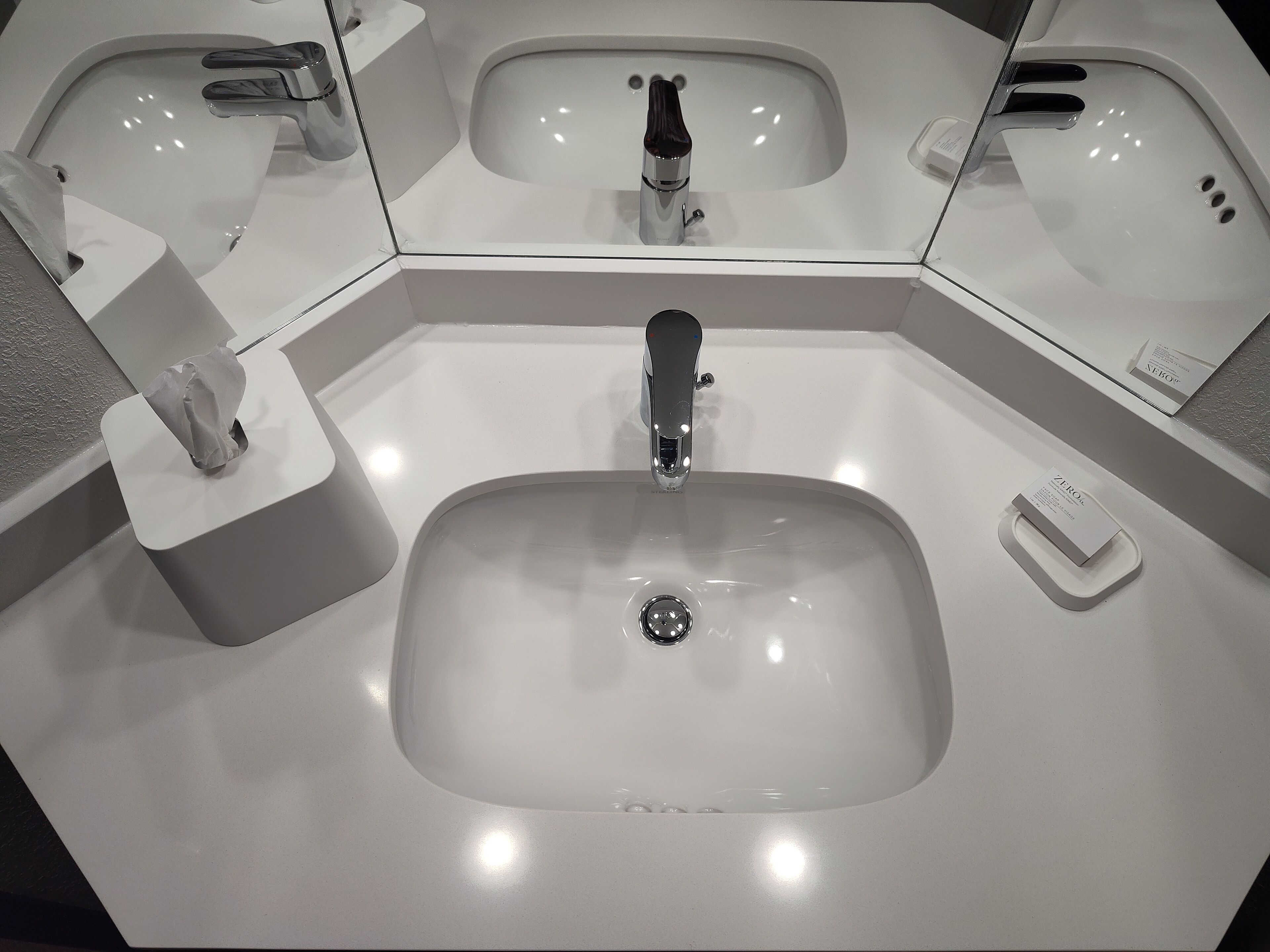 A modern bathroom with a large sink, a mirror, and a hand dryer.