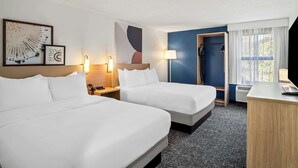 A hotel room with two beds, a desk, a chair, a lamp, and artwork on the wall.