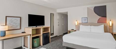 Une chambre d’hôtel équipée d’un lit, d’un bureau, d’une télévision, d’un miroir et d’un mur décoré d’œuvres d’art abstraites.