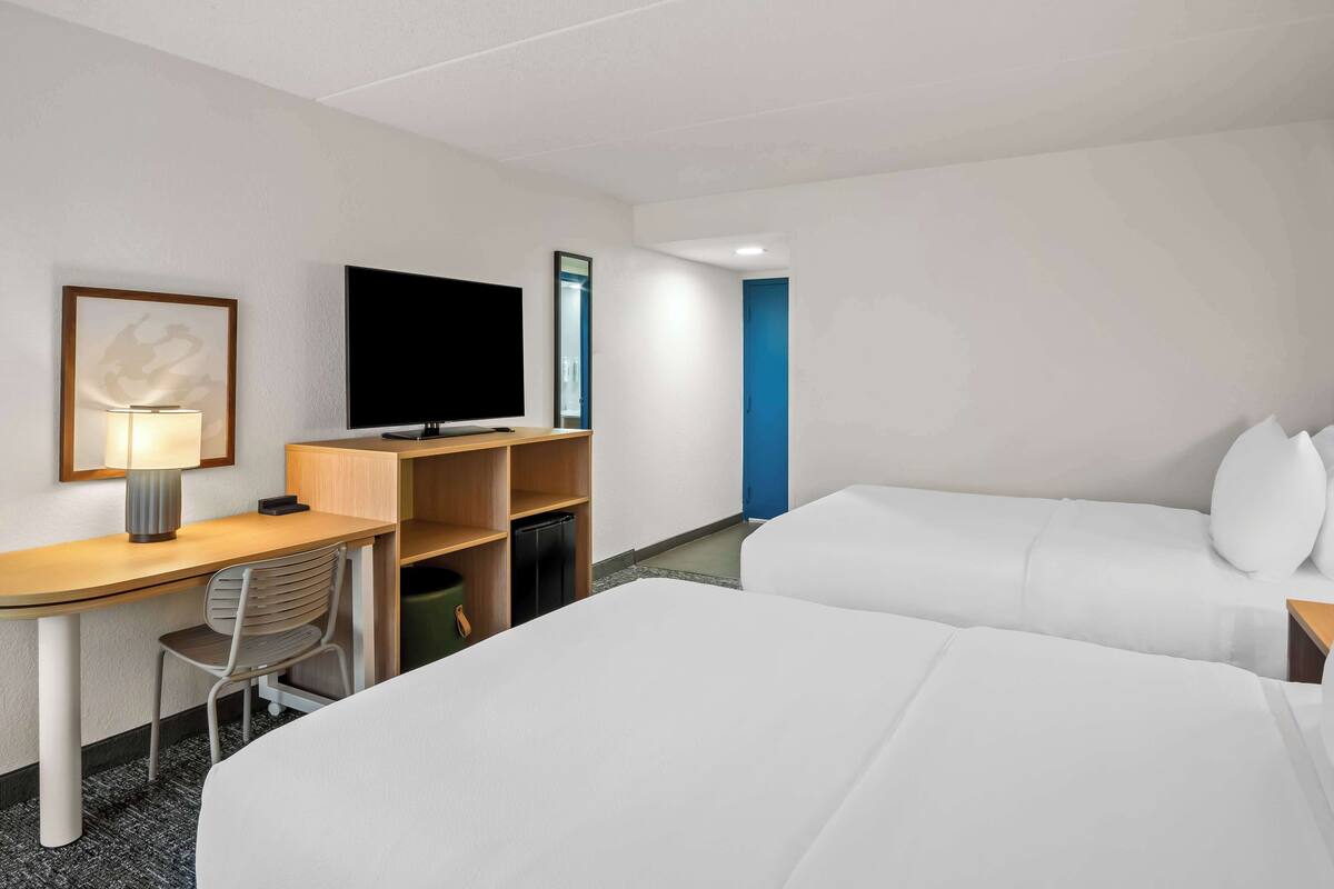 Ett hotellrum med ett skrivbord, en platt-TV, en säng och en blå dörr.