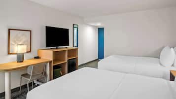A hotel room with a desk, a flat-screen TV, a bed, and a blue door.