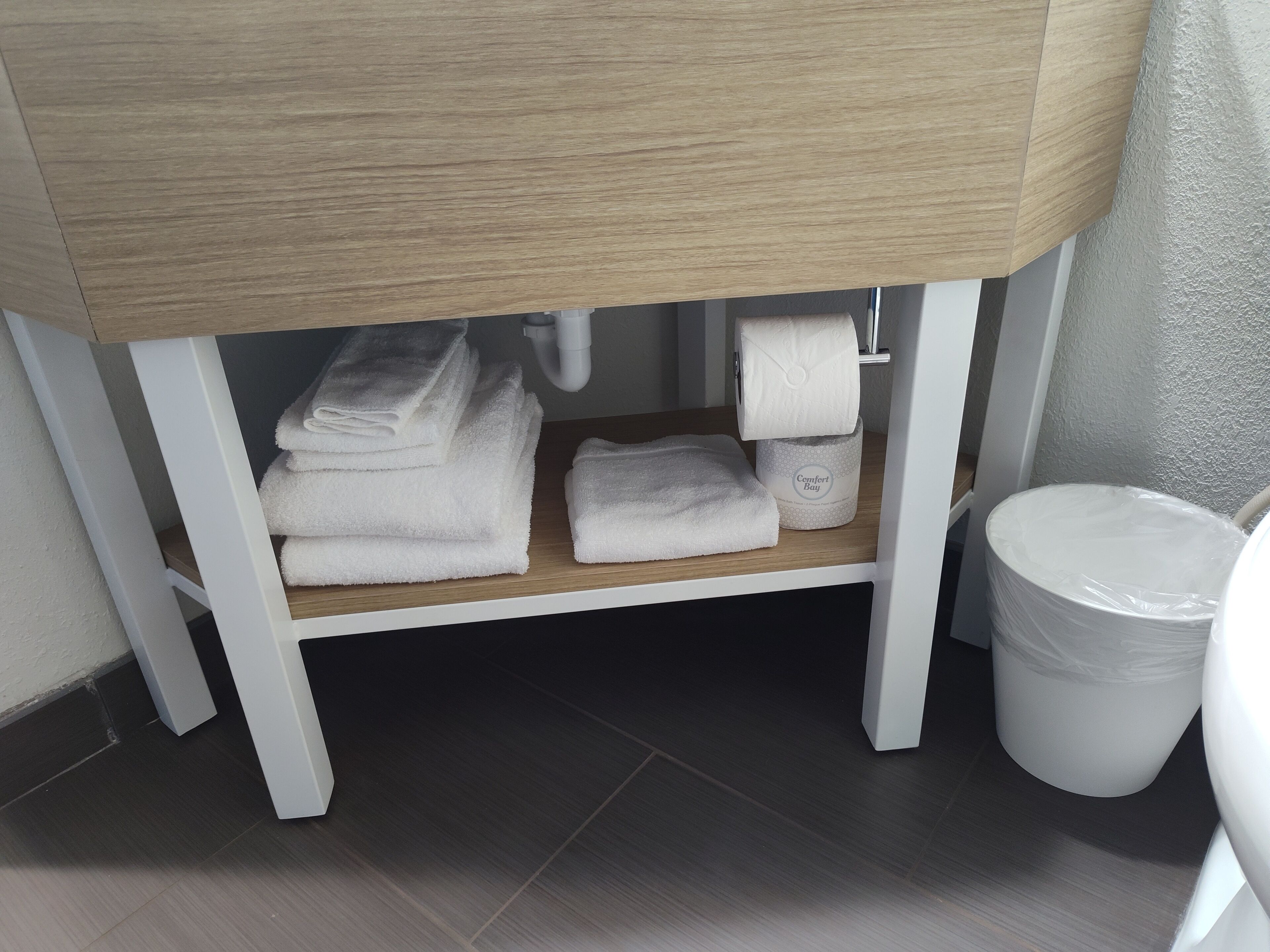 A bathroom vanity with a wooden countertop, a white sink, and a white trash bin.