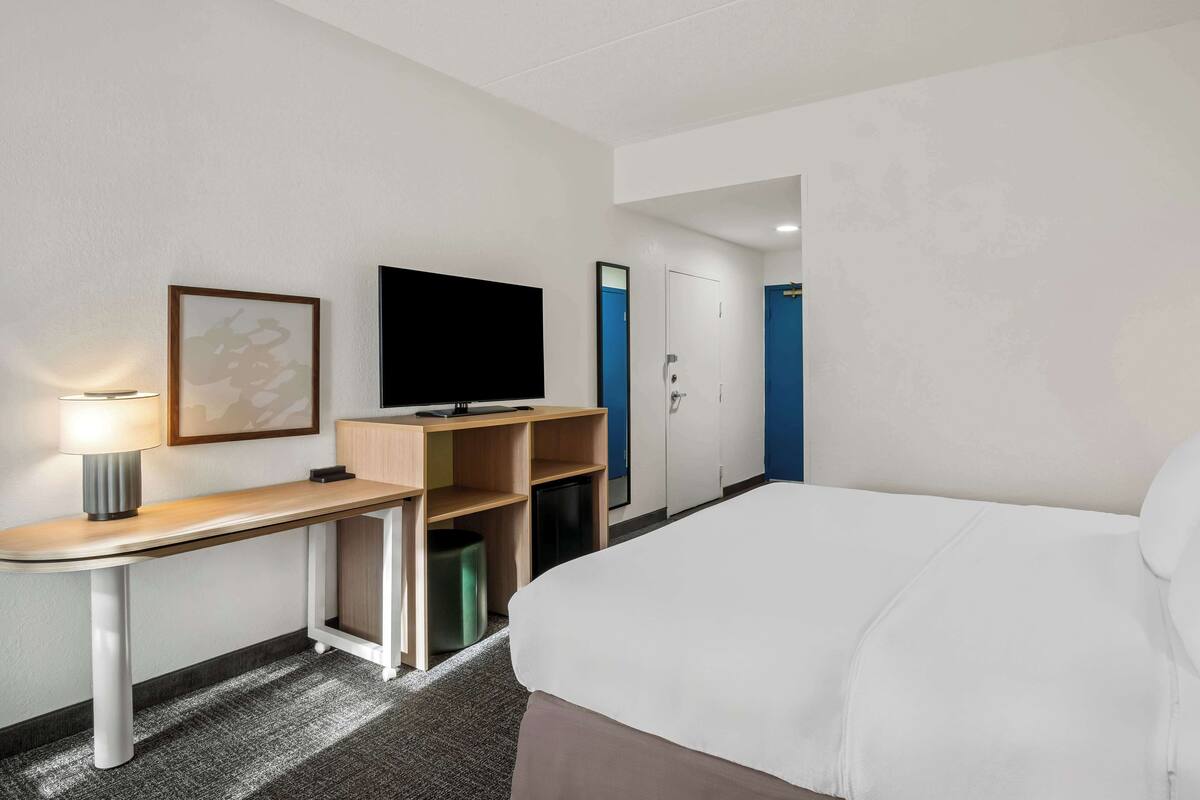 Ett hotellrum med en säng, ett skrivbord med en lampa, en tv och en garderob.