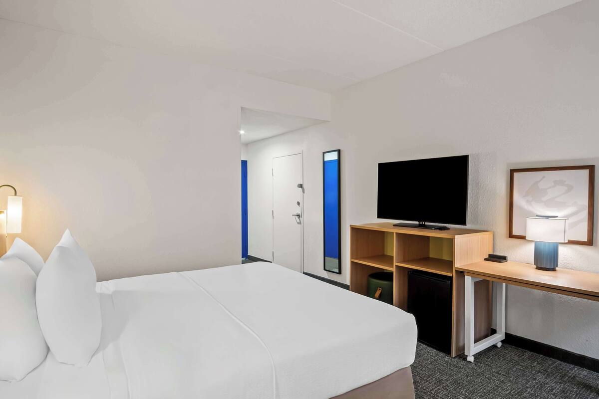 Ett hotellrum med en säng, ett skrivbord med en tv, en lampa och en dörr med en blå detalj.
