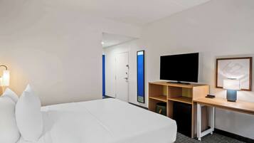 A hotel room with a bed, a desk with a television, a lamp, and a door with a blue accent.