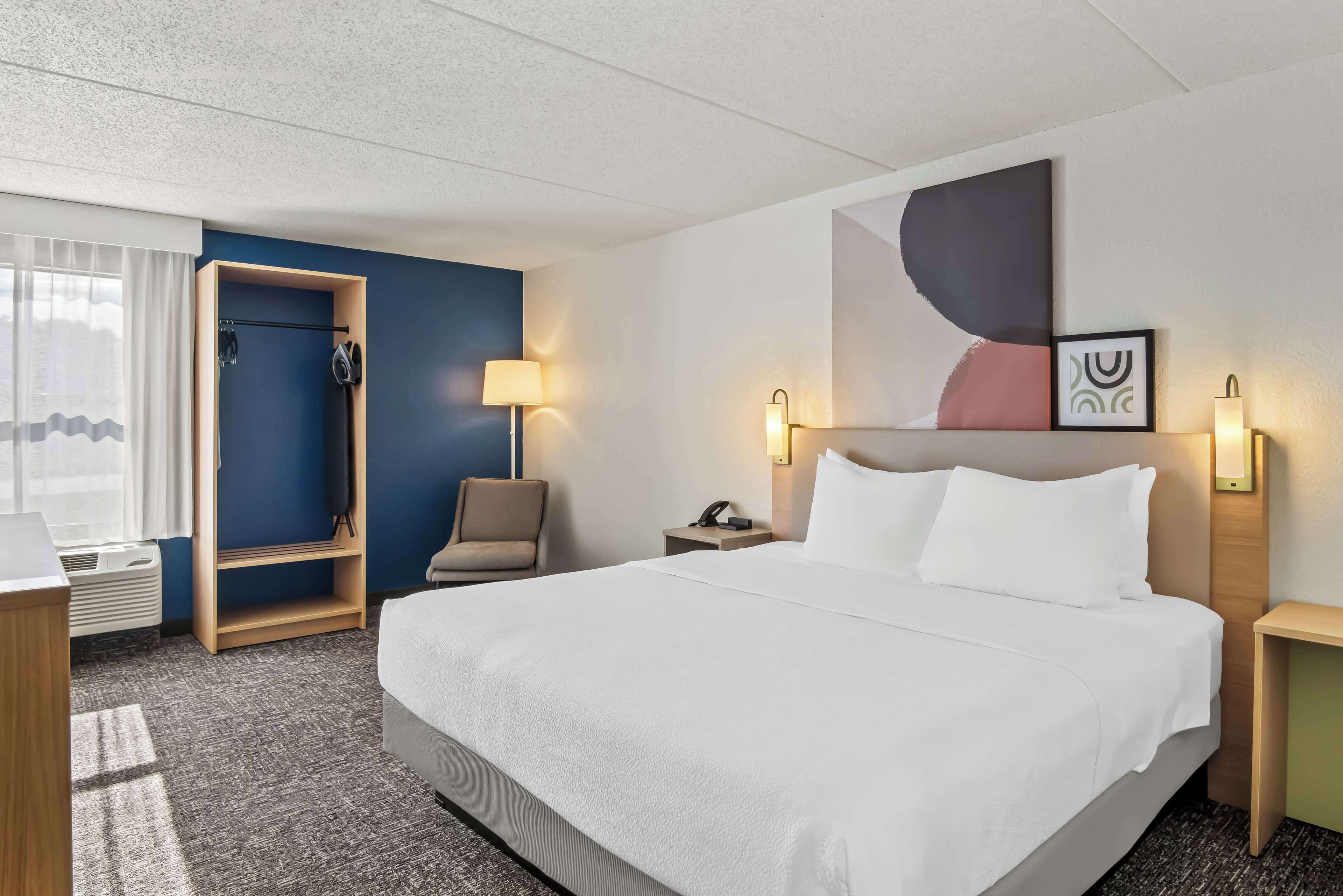 A hotel room with a large bed, a desk, a chair, a wardrobe, and a window with curtains.