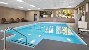 An indoor swimming pool with clear water, a metal ladder, and a bench area with chairs.
