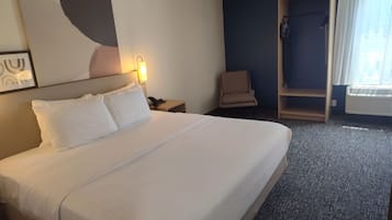 Habitación de hotel con una cama grande, una silla, un escritorio con teléfono, una lámpara de pared y una ventana con cortinas.